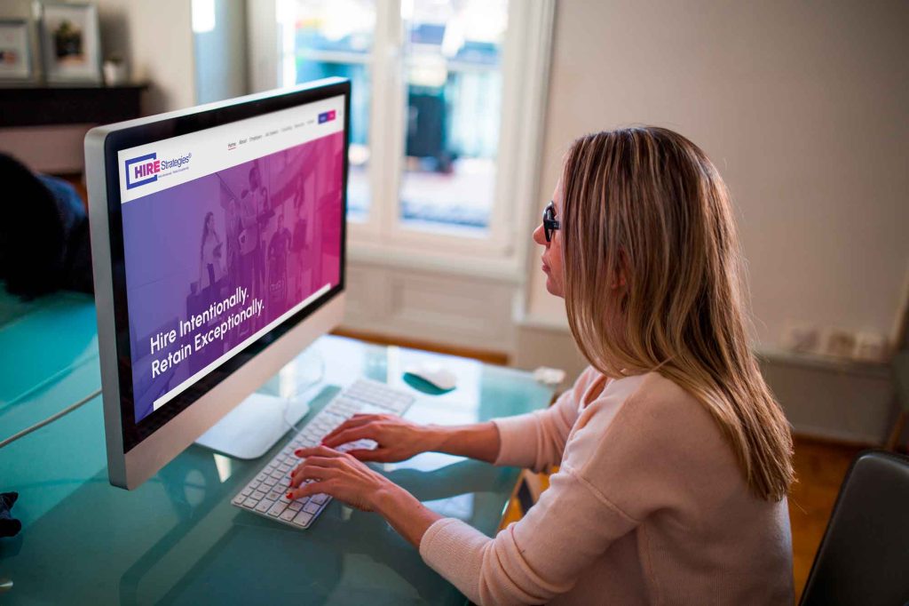 woman looking at HIRE Strategies website on desktop computer